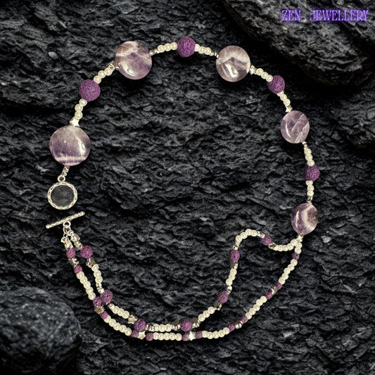 This lightweight bohemian necklace is displayed on a dark textured stone background that highlights the glossy lavender beads and delicate white accents. The double-strand arrangement creates layered texture and movement inspired by elegant handmade gemstone jewellery styling.