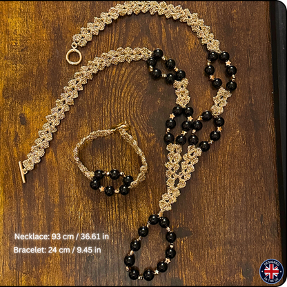 A handmade macrame jewelry set consisting of a necklace and bracelet, displayed on a dark wood background. The jewelry features intricate tan macrame woven patterns accented with black beads and small gold star details.