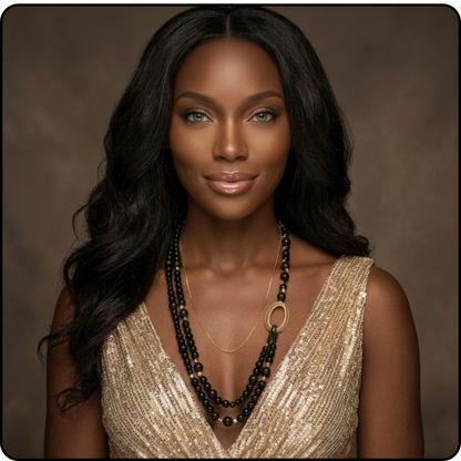 A woman with long, wavy black hair is shown from the chest up against a warm brown studio background. She is wearing layered necklaces, including a prominent black beaded necklace with a gold oval pendant and a delicate gold chain, along with a gold sequined top.