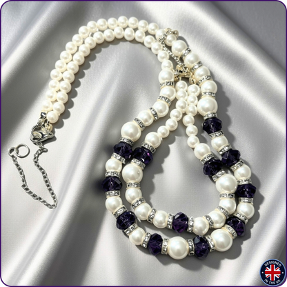 A multi-strand pearl necklace with dark purple faceted beads and silver crystal spacers, displayed on a shiny silver satin background.