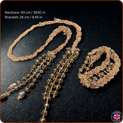 A jewelry set on a dark textured background, featuring a long beaded necklace and a matching bracelet. The necklaces and bracelets have a textured bronze or gold-toned metal base with cascading strands of faceted brown and smoky amber beads.