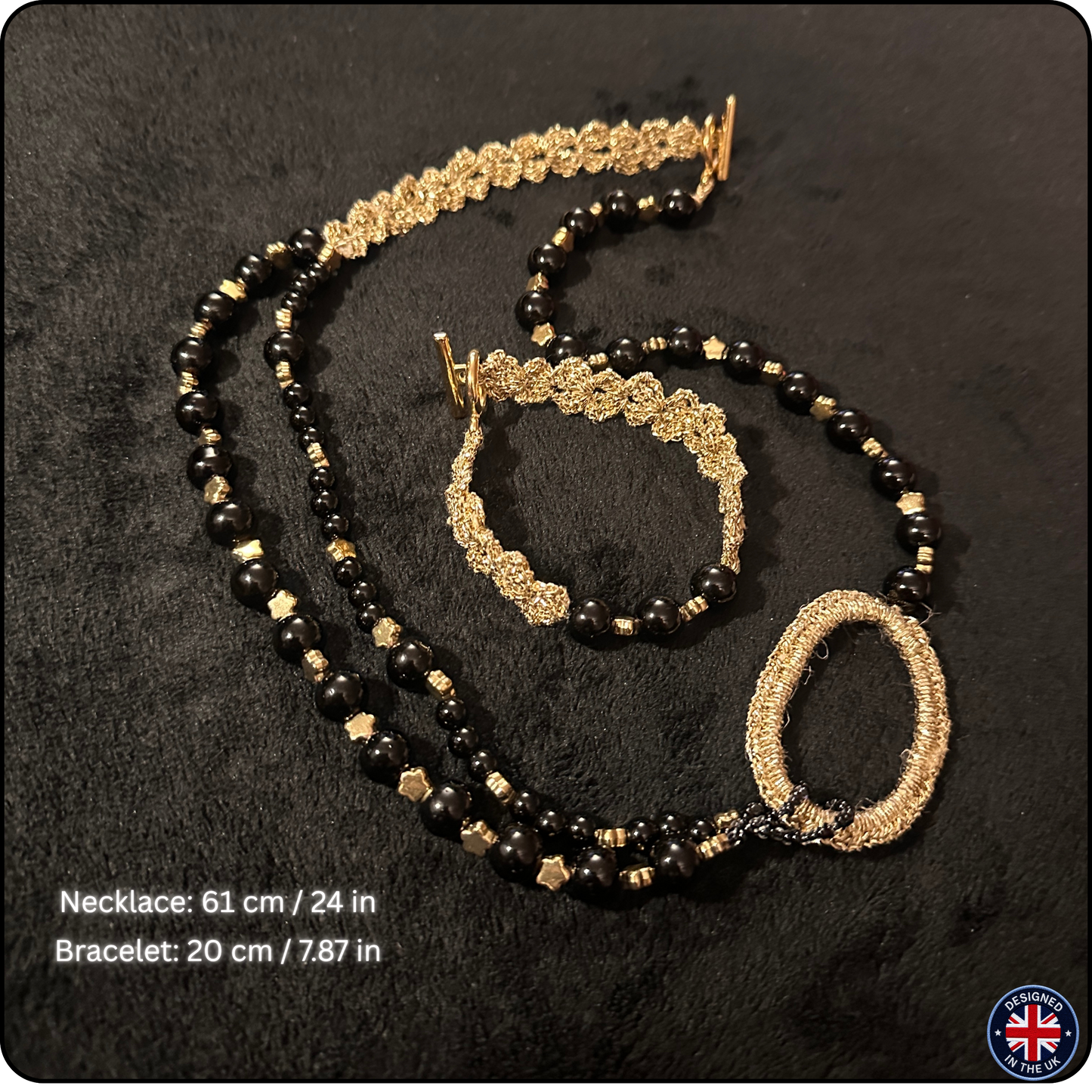 A black and gold beaded jewelry set consisting of a necklace and bracelet, displayed on a black textured background. The necklace features black beads, gold star-shaped beads, and a large textured gold oval centerpiece.