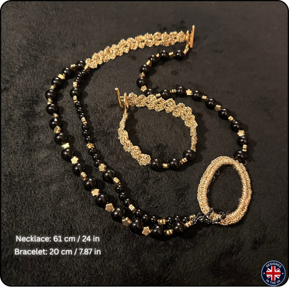 A black and gold beaded jewelry set consisting of a necklace and bracelet, displayed on a black textured background. The necklace features black beads, gold star-shaped beads, and a large textured gold oval centerpiece.