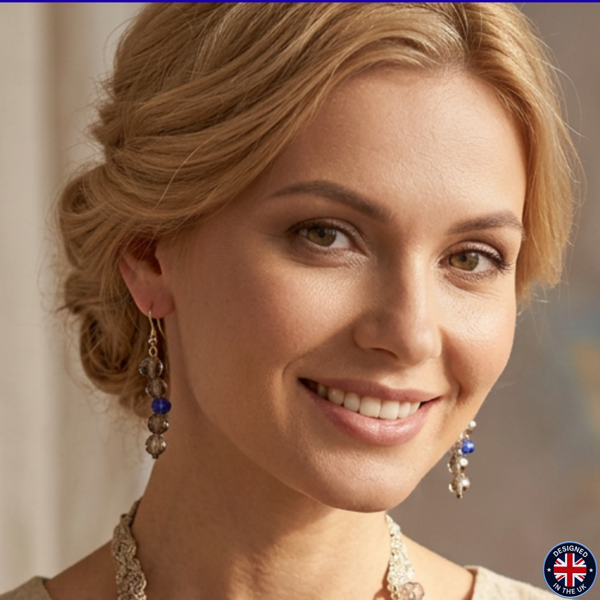 A close-up portrait of a smiling blonde woman wearing dangling beaded earrings with blue and silver beads, along with a necklace. A small 'Made in the UK' badge appears in the bottom right corner.