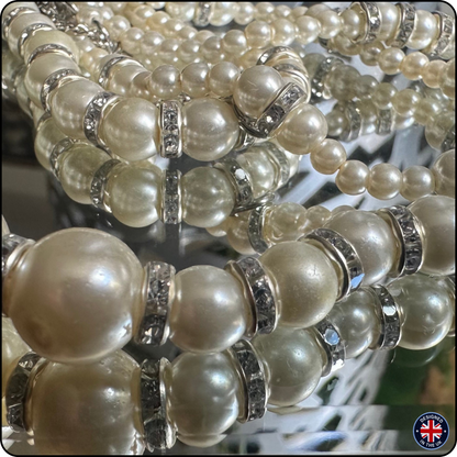 Close-up of multiple strands of pearl beaded bracelets with silver spacer rings, displayed on a reflective surface.