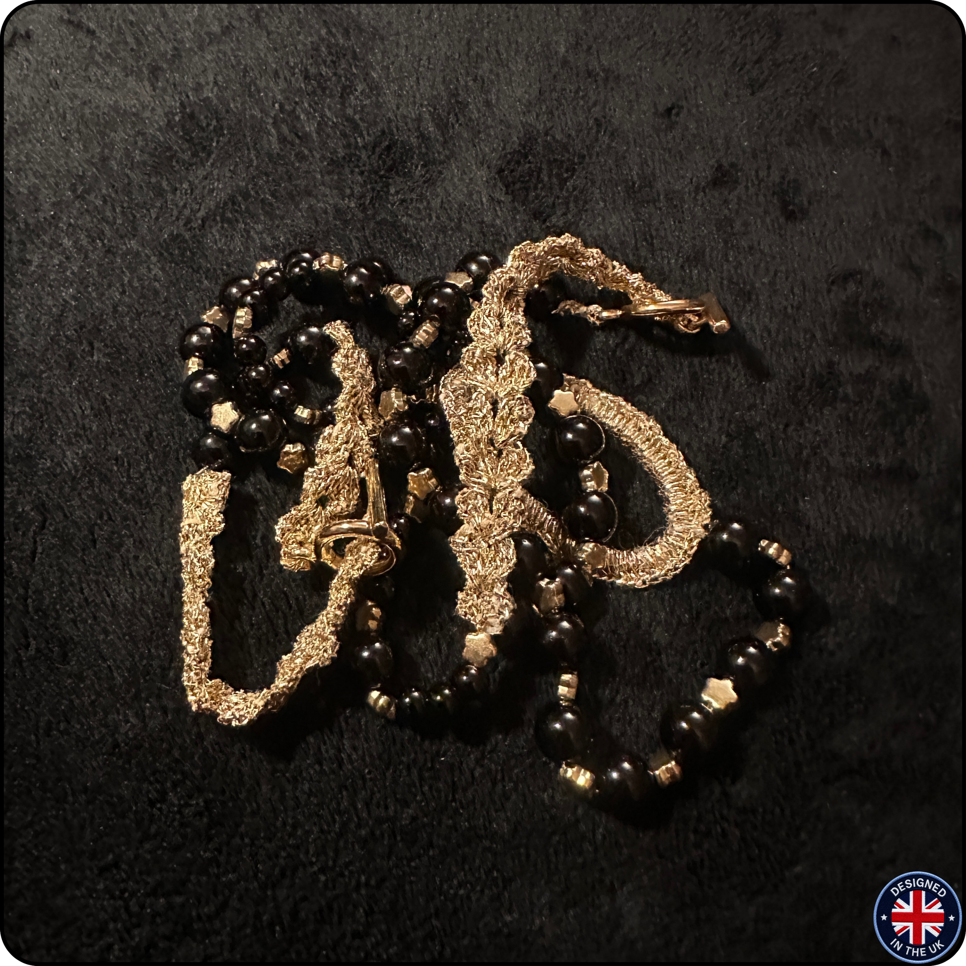 A vintage-style necklace featuring black faceted beads and textured gold-toned metal chains, displayed on a dark textured background.