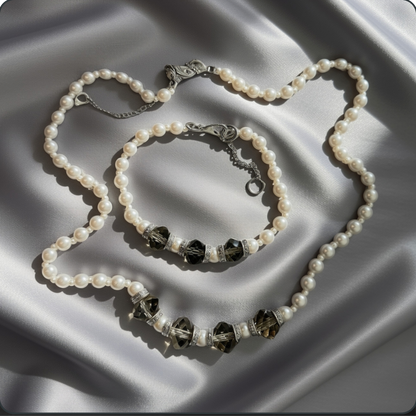 A pearl-bead necklace and matching bracelet with dark faceted crystal beads and silver-toned accents, arranged on draped satin fabric.