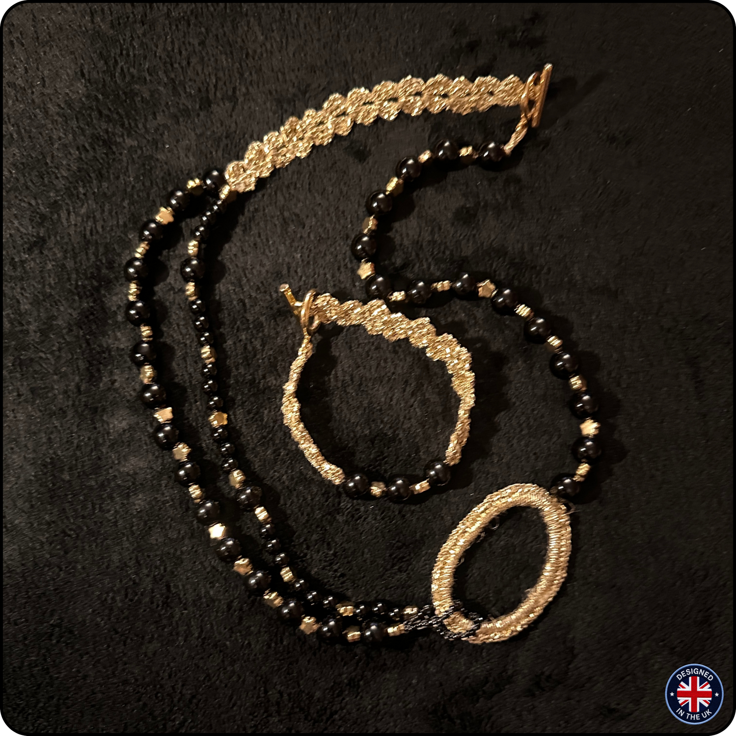 A jewelry set featuring a beaded necklace, bracelet, and matching headband laid out on a black textured background. The beads alternate between glossy black and metallic gold, with gold-toned woven details on the clasp, ends, and bracelet.