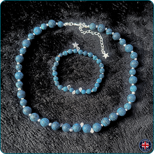 A jewelry set featuring a beaded necklace and matching bracelet in textured blue stone with silver star charms, displayed on a black textured background.