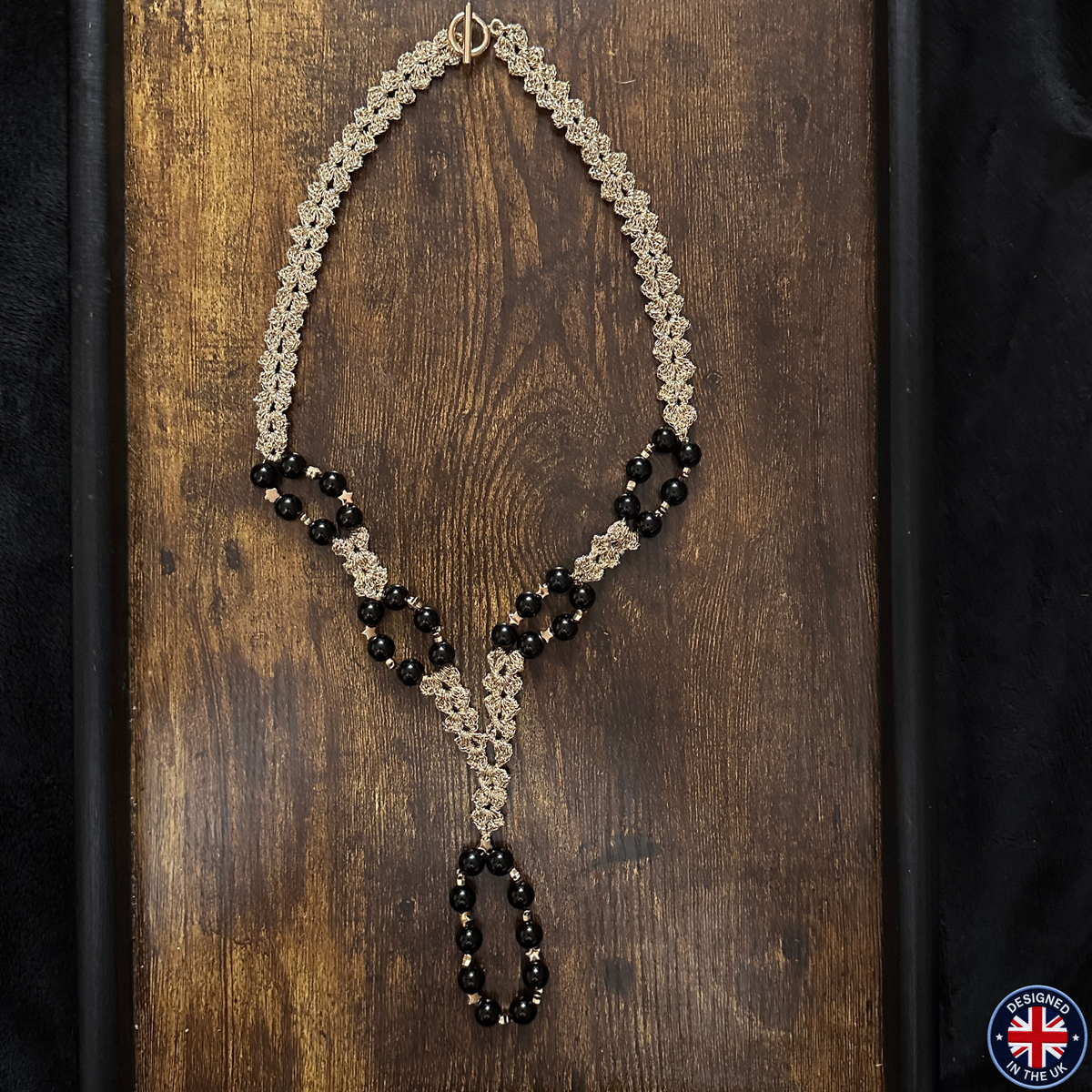 A handmade beaded necklace with a gold-tone chain and black beads, displayed on a dark wooden background.