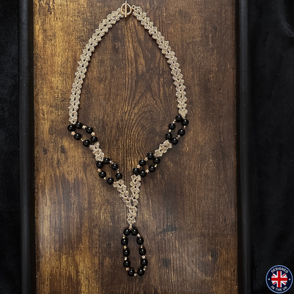 A handmade beaded necklace with a gold-tone chain and black beads, displayed on a dark wooden background.