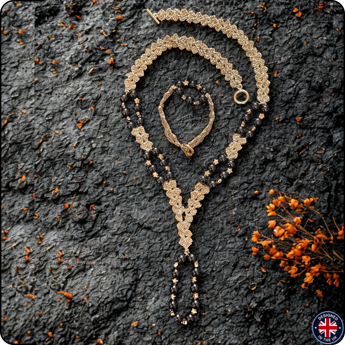 A gold and black beaded necklace with a matching bracelet, styled on a dark textured stone background with dried orange flowers. A circular 'Made in UK' badge is in the bottom right corner.