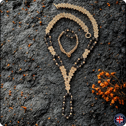 A gold and black beaded necklace with a matching bracelet, styled on a dark textured stone background with dried orange flowers. A circular 'Made in UK' badge is in the bottom right corner.