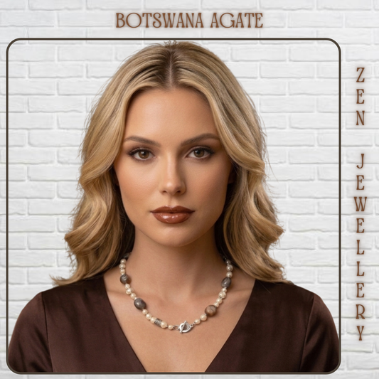 A woman with blonde hair models a Botswana agate jewelry necklace against a white brick wall background. The necklace features natural brown and gray agate stones with a silver-toned central charm.
