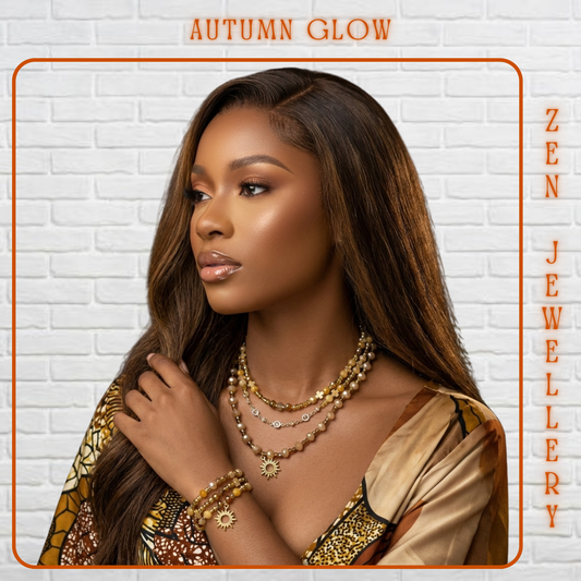 A woman with long dark brown hair models layered gold and silver jewelry, including necklaces, bracelets, and earrings, against a white brick wall background. The image features orange text reading 'AUTUMN GLOW' at the top and 'ZEN JEWELLERY' vertically on the right side.