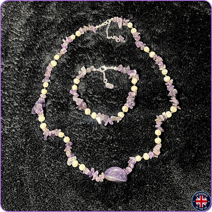 Amethyst crystal jewelry set including a necklace and bracelet, displayed on a black textured background. The jewelry features light purple amethyst chips, lavender beads, and a larger polished purple stone centerpiece on the necklace.