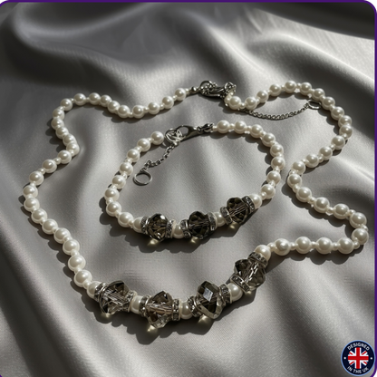 A pearl necklace and matching bracelet with faceted gray beads and silver-toned chain details, arranged on draped satin fabric.