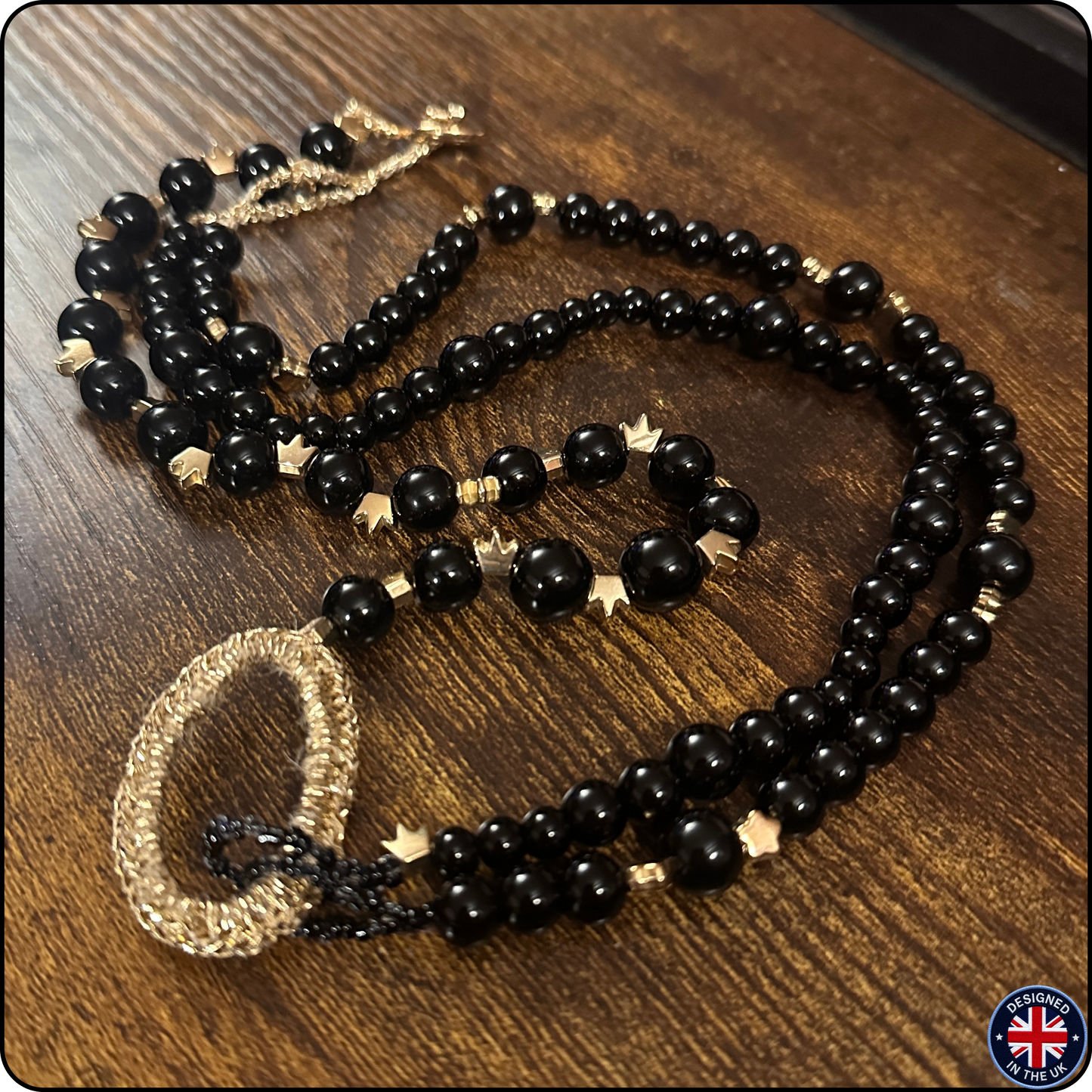 A black beaded necklace with gold-toned star and textured bead accents, displayed on a dark wooden surface.