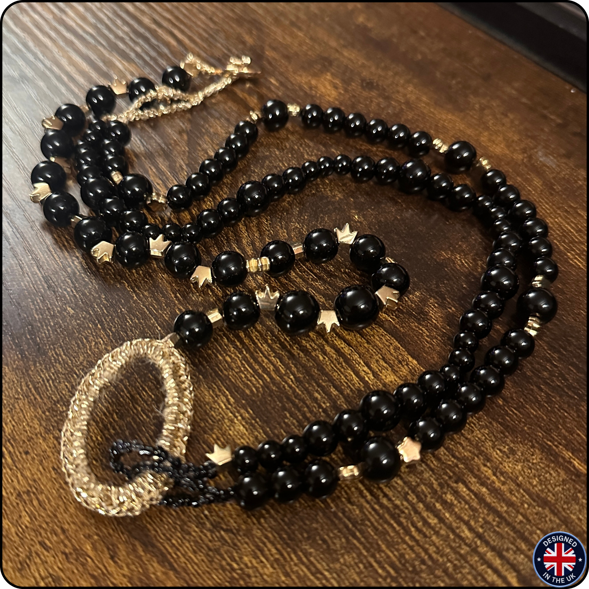 A black beaded necklace with gold-toned star and textured bead accents, displayed on a dark wooden surface.