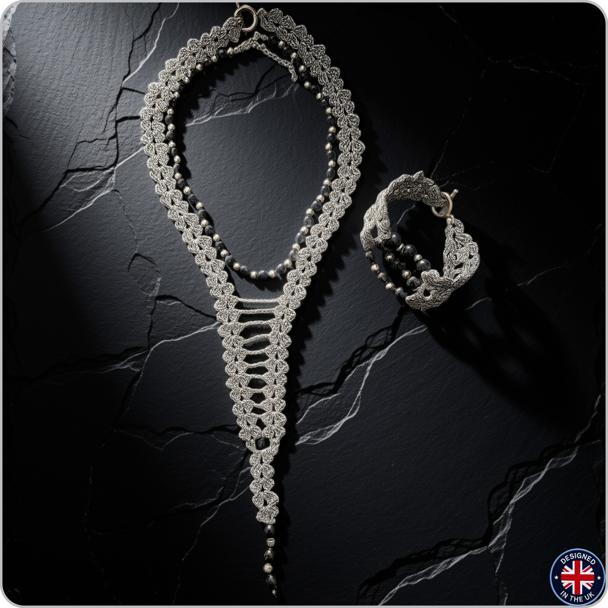 A silver-toned crochet lace jewelry set featuring a long necklace and a matching bracelet, displayed on a dark textured stone surface.