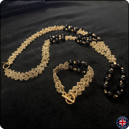 A jewelry set featuring a gold-tone chain necklace, bracelet, and matching rings with black faceted beads, displayed on a black velvet background.