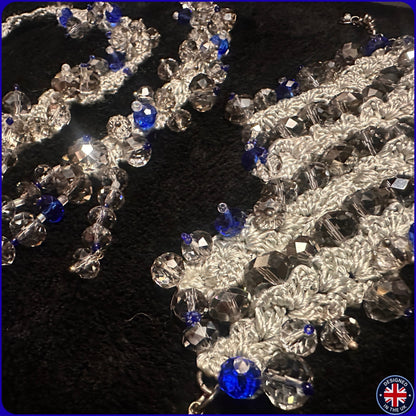 A close-up of a beaded embellishment or trim featuring clear faceted crystal beads and bright blue beads woven onto a silver crochet.
