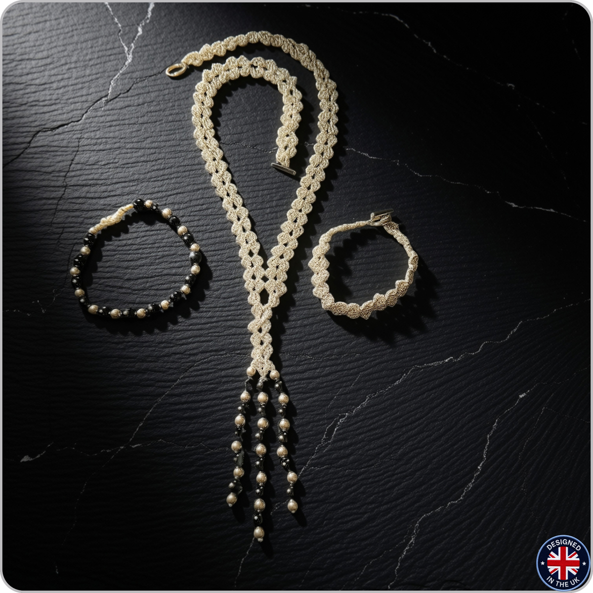 A handmade jewelry set featuring a cream-colored crocheted lariat necklace, a matching crocheted bracelet, and a black beaded bracelet, displayed on a dark textured background.
