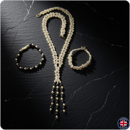 A handmade jewelry set featuring a cream-colored crocheted lariat necklace, a matching crocheted bracelet, and a black beaded bracelet, displayed on a dark textured background.