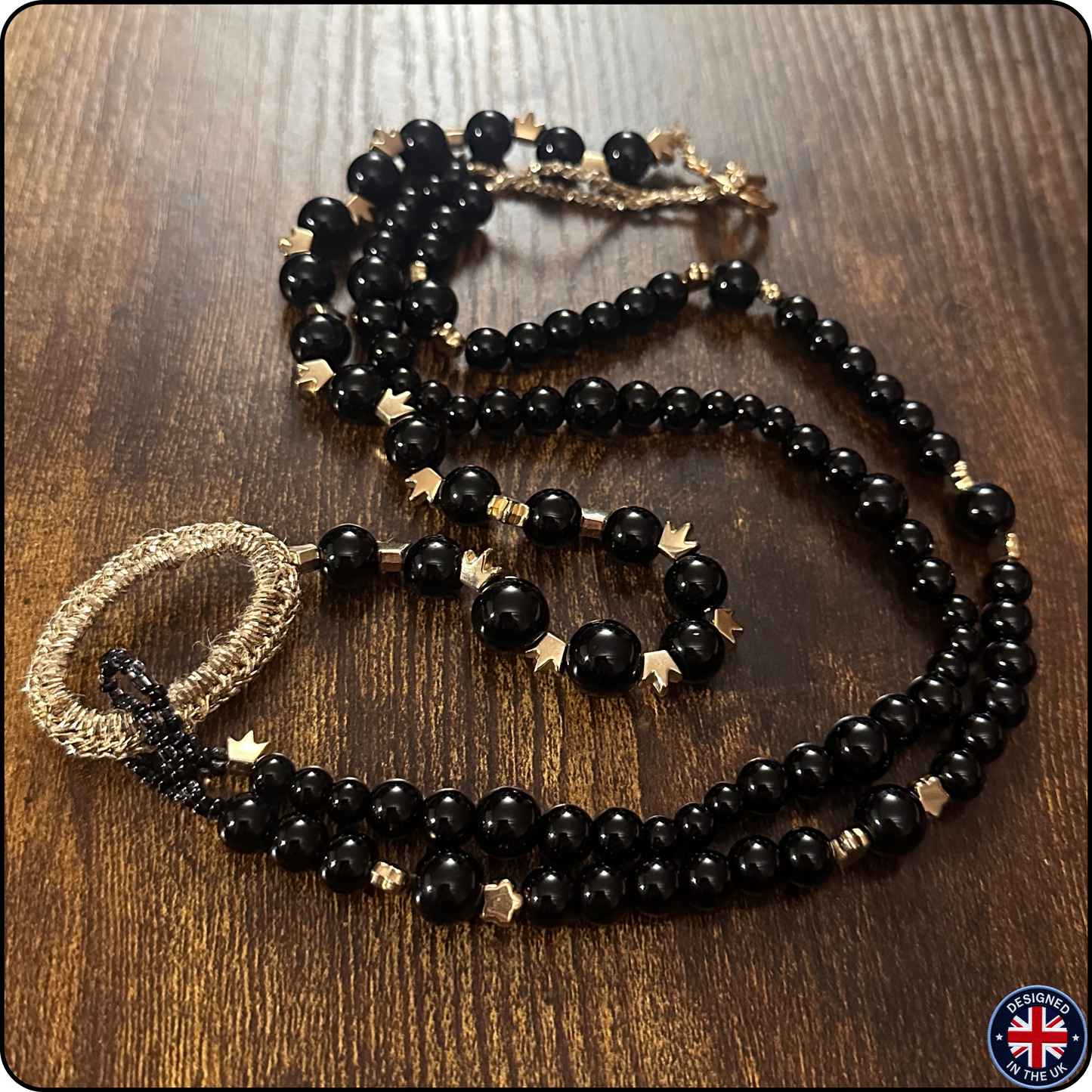 A beaded necklace with large glossy black beads, small gold star-shaped spacers, and a chunky gold woven ring clasp, displayed on a dark wood surface.
