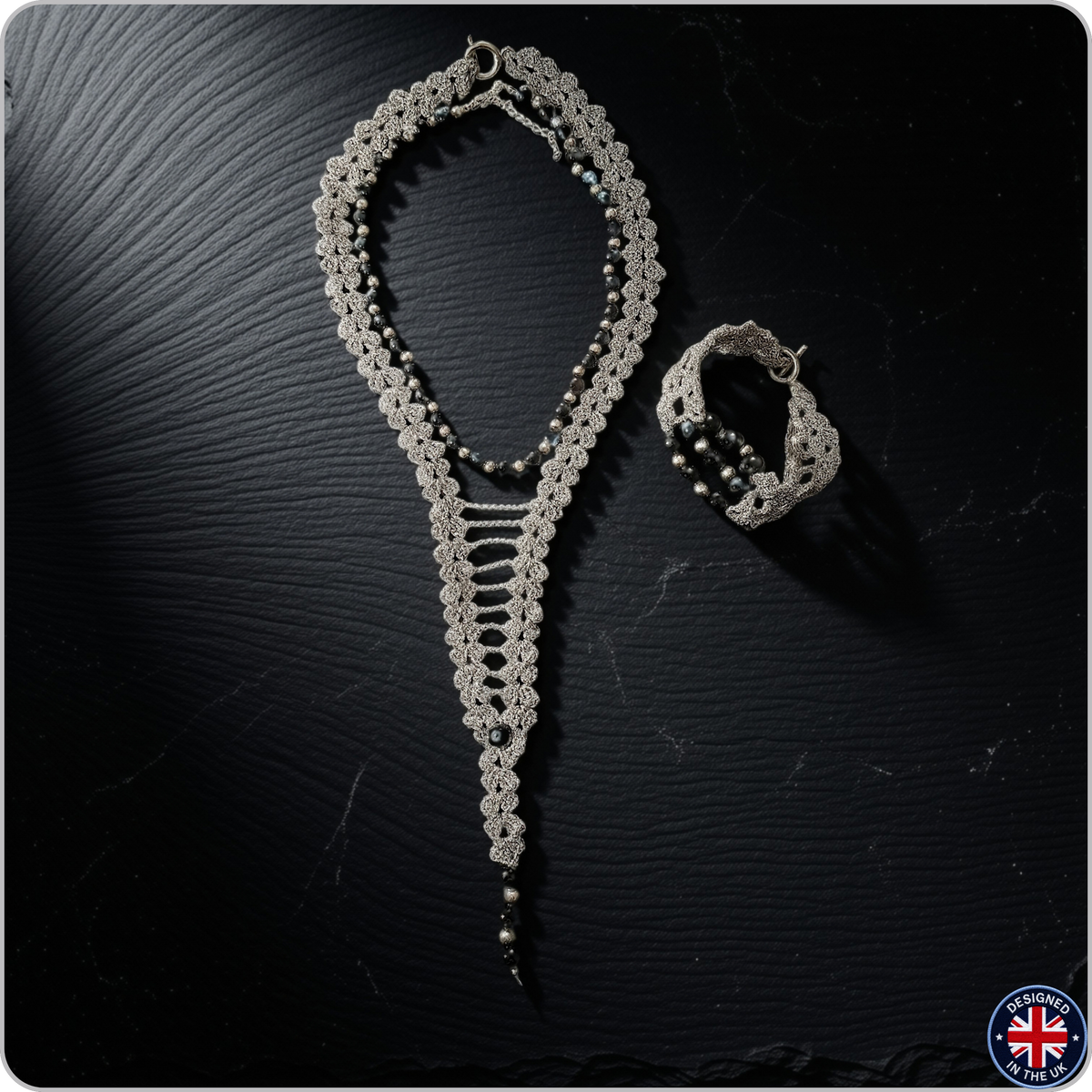 A silver-toned crochet jewelry set featuring a long beaded necklace and a matching bracelet, displayed on a dark textured background.