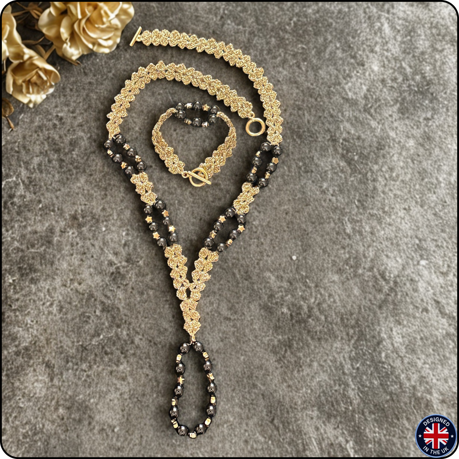 A gold and black beaded necklace set with a matching bracelet, displayed on a textured gray background with decorative gold flowers in the corner.