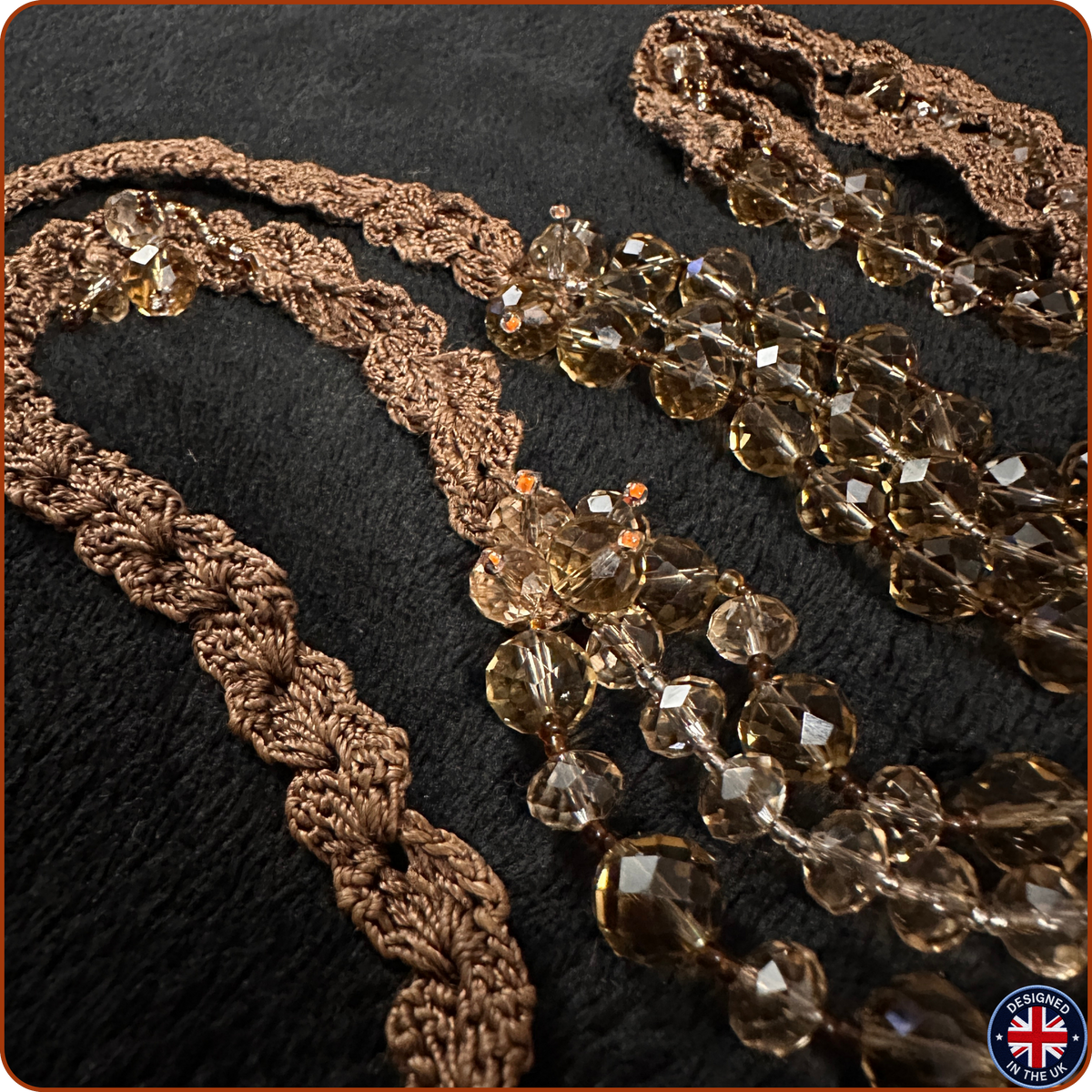 A close-up of a brown crocheted lace trim with faceted clear beads, laid out on a black textured background. 