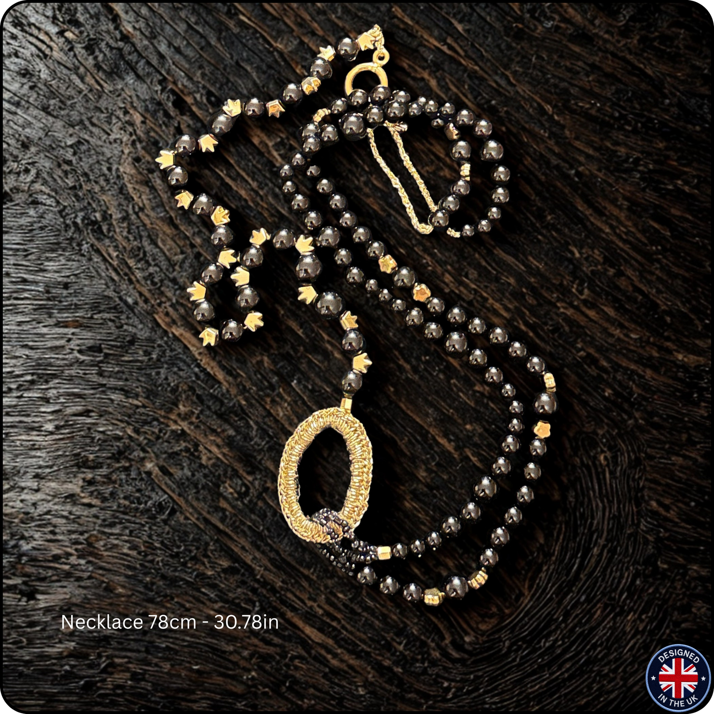 A beaded necklace with dark gray faceted beads, gold star accents, and a large oval pendant covered in small clear stones, displayed on a dark wood background. Text at the bottom reads 'Necklace 78cm - 30.