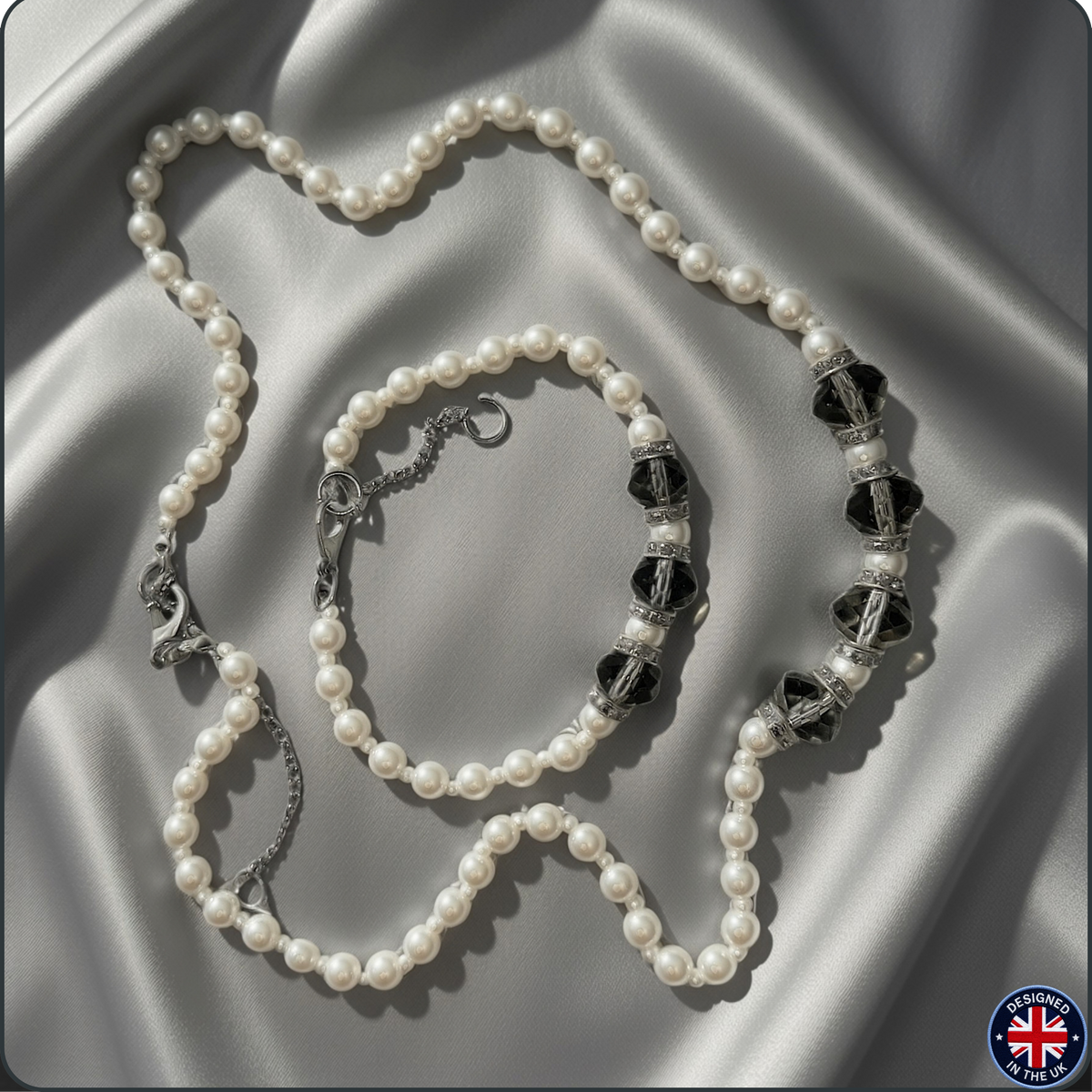 A pearl beaded necklace with black faceted beads and silver-toned metal accents, arranged on draped satin fabric.
