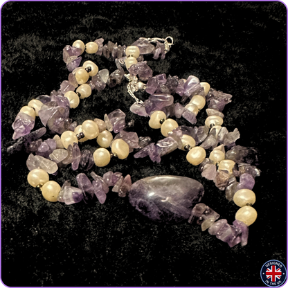 A beaded necklace featuring irregular purple amethyst chips and smooth cream-colored pearl-like beads, with a polished oval purple stone centerpiece, displayed on a black textured background.