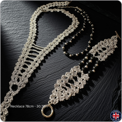A silver-toned beaded necklace with a matching ornate lace-style pendant and a separate strand of dark beads, arranged on a dark textured surface. White text at the bottom left reads 'Necklace 78cm - 30.