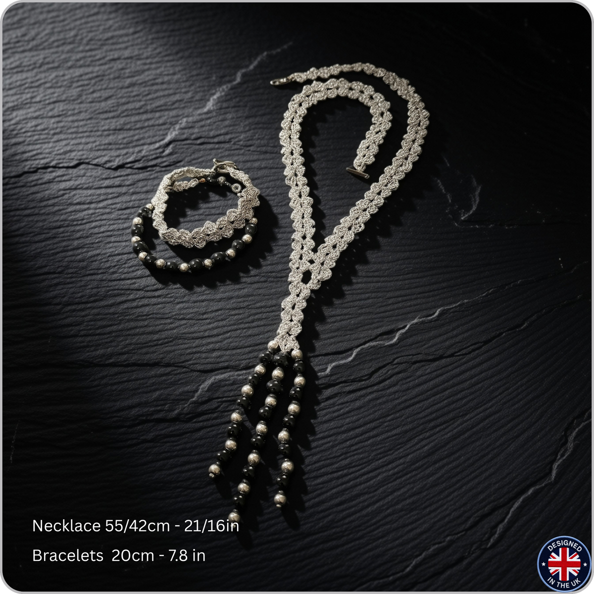 A silver-toned beaded necklace and matching beaded bracelets displayed on a dark textured background. Text at the bottom reads 'Necklace 55/42cm - 21/16in' and 'Bracelets 20cm - 7.