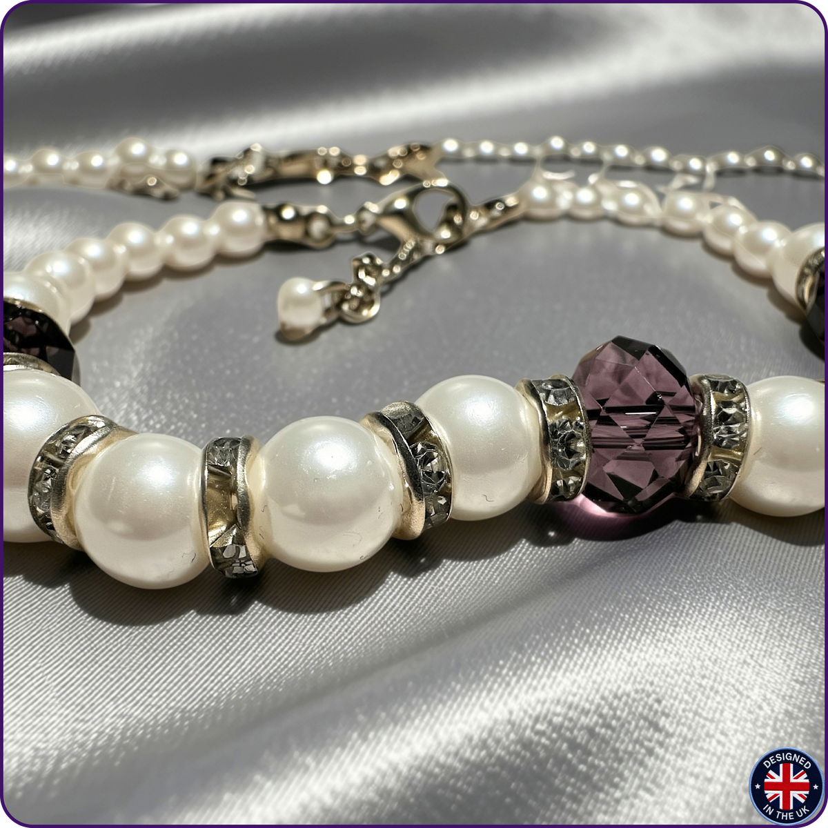 A pearl beaded bracelet with silver-toned metal spacers and a faceted dark purple crystal centerpiece, displayed on a silver satin fabric background.