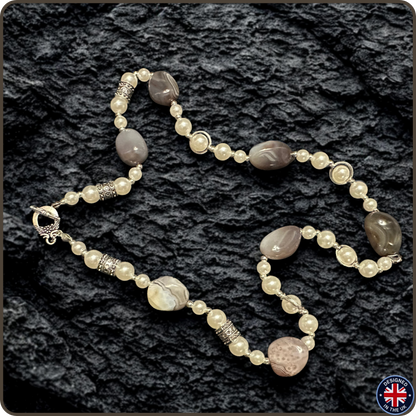 A beaded necklace with cream pearl-like beads, polished taupe stone beads, and silver-toned spacer beads, displayed on a dark textured background.