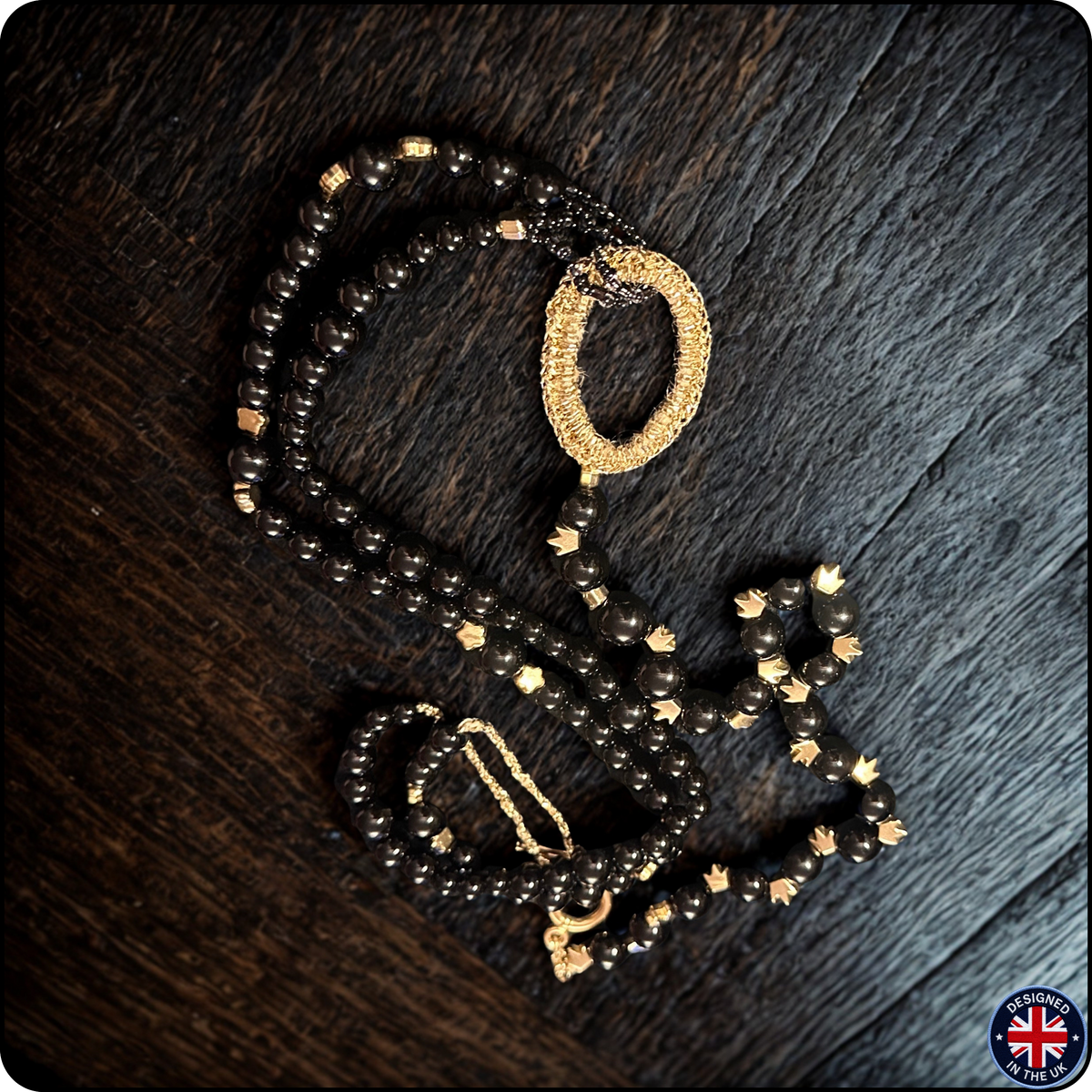 A beaded necklace with dark brown faceted beads and gold-toned accents, including a textured gold ring and a gold chain detail, displayed on a dark wood background.