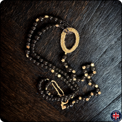A beaded necklace with dark brown faceted beads and gold-toned accents, including a textured gold ring and a gold chain detail, displayed on a dark wood background.