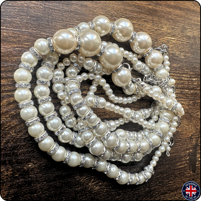 A multi-strand pearl necklace with large and small cream-colored pearls, accented by silver-toned beads with clear rhinestones, displayed on a dark wood background.