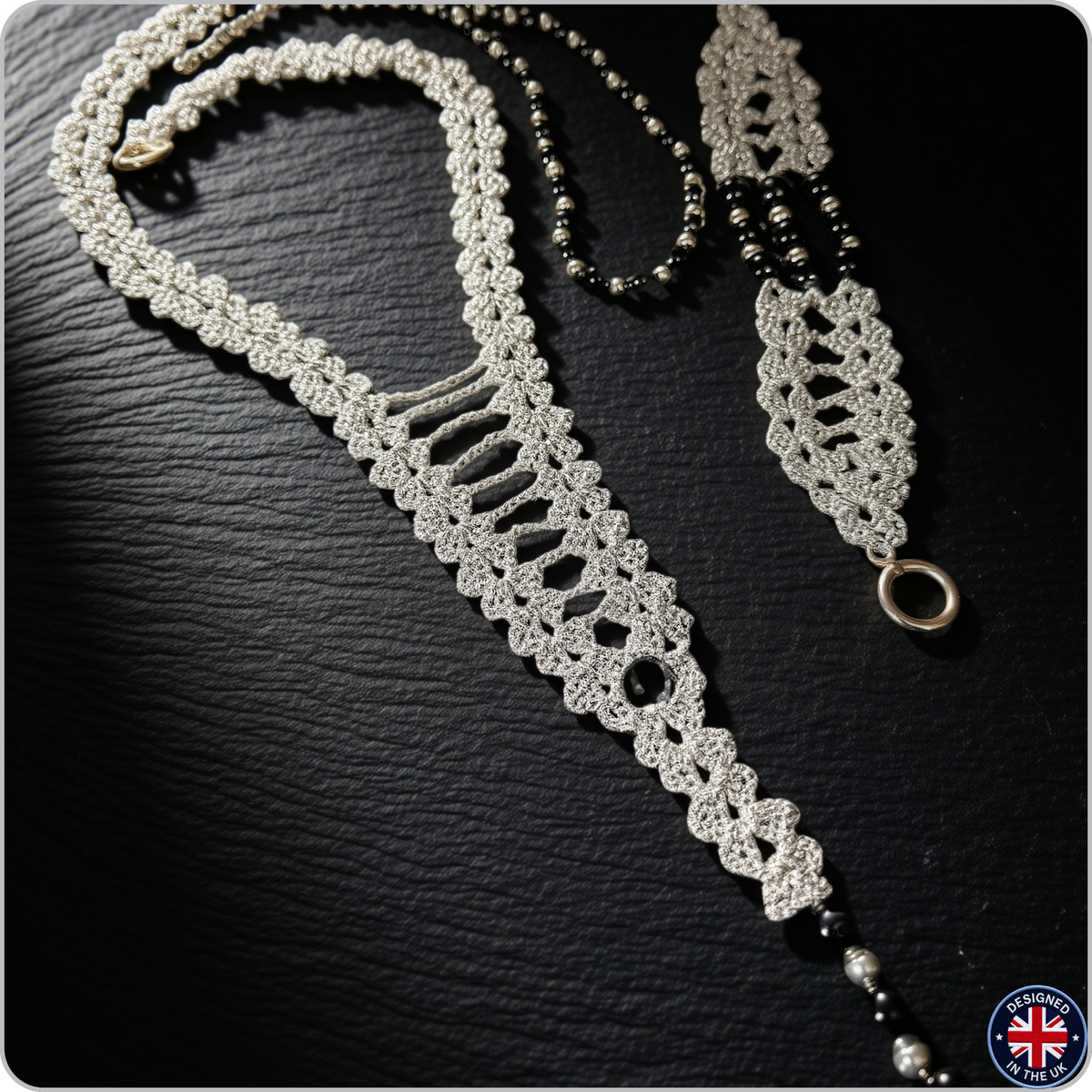 A handmade macrame-style necklace with a silver-toned woven body, black beads, and a silver-toned ring clasp, displayed on a dark textured background.