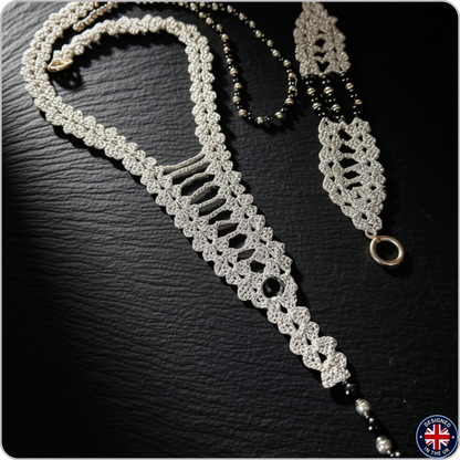 A handmade macrame-style necklace with a silver-toned woven body, black beads, and a silver-toned ring clasp, displayed on a dark textured background.