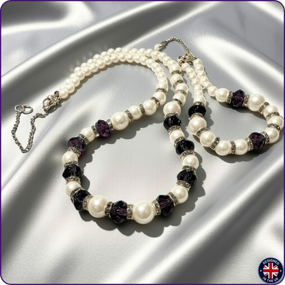 A beaded necklace and matching bracelet displayed on draped silver satin fabric. The jewelry features white faux pearls, faceted dark purple crystal beads, and silver-toned spacer rings with small clear rhinestones.