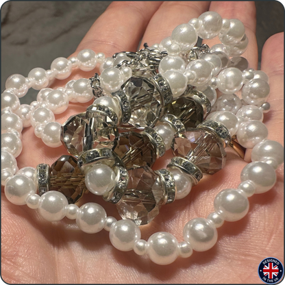 A close-up of a hand holding a strand of white faux-pearl beads with faceted clear crystal spacers and silver-toned metal rings. A small circular 'Made in UK' badge is visible in the bottom right corner.