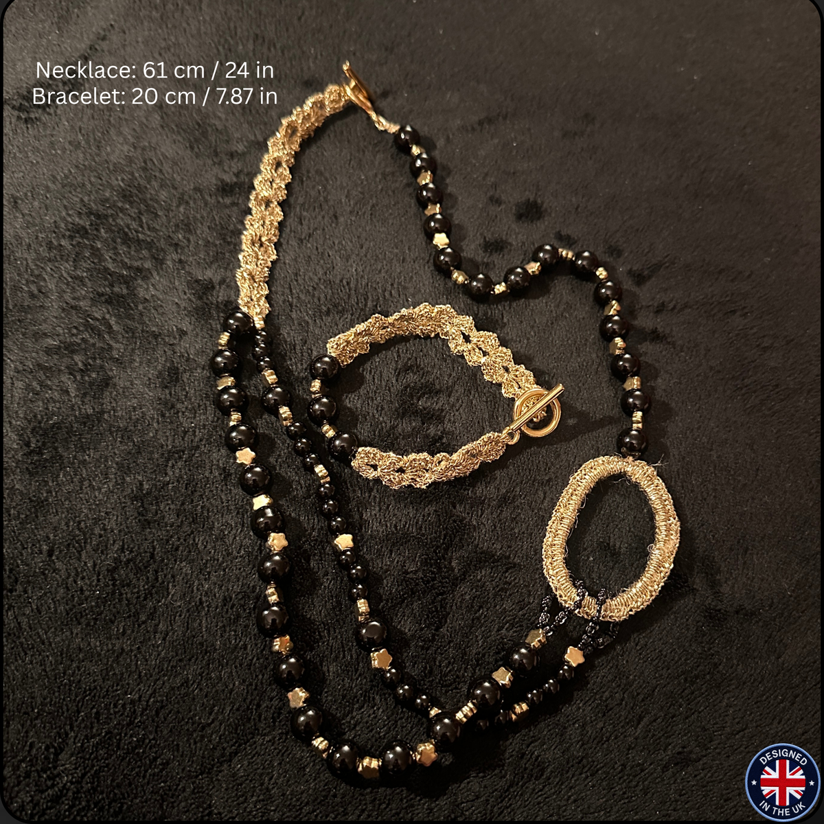 A jewelry set featuring a long beaded necklace and a matching bracelet, displayed on a dark textured background. The jewelry has black faceted beads, gold-toned spacer beads, and a gold-toned woven chain detail.