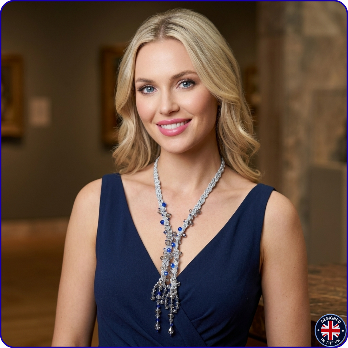 A blonde woman in a navy blue dress wearing an elaborate silver-toned statement necklace with blue and clear stones, set against a blurred indoor background.