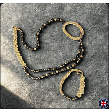 A gold and black beaded jewelry set consisting of a double-strand necklace and a matching bracelet, displayed on a textured gray background.