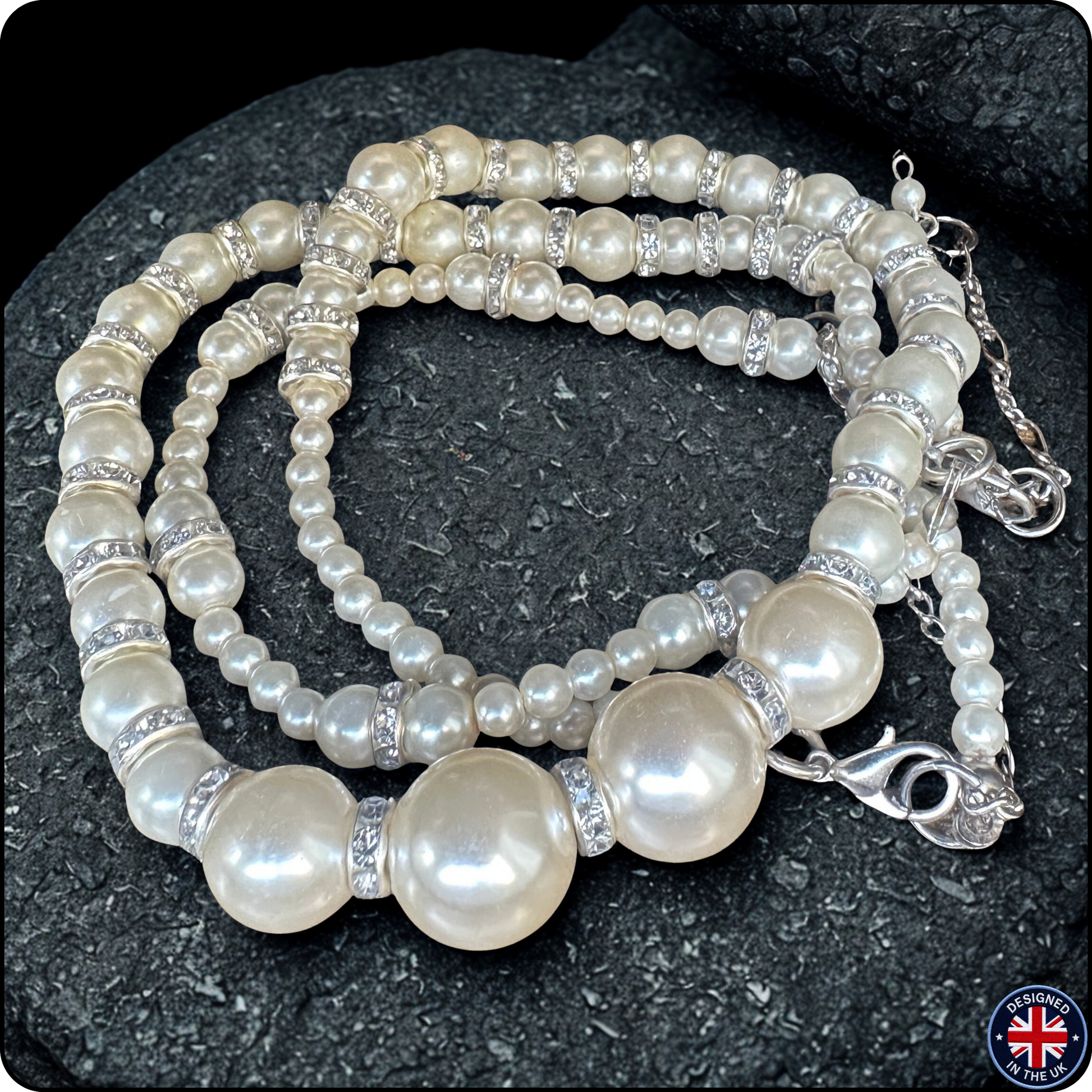 A multi-strand pearl beaded necklace with silver-toned spacer beads and a lobster clasp, displayed on a dark textured rock background.